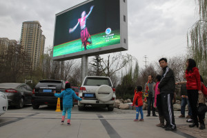 A young girl copies a dancer on a video billboard in a park on the banks of the Yellow River in Lanzhou, Gansu Province, North West China